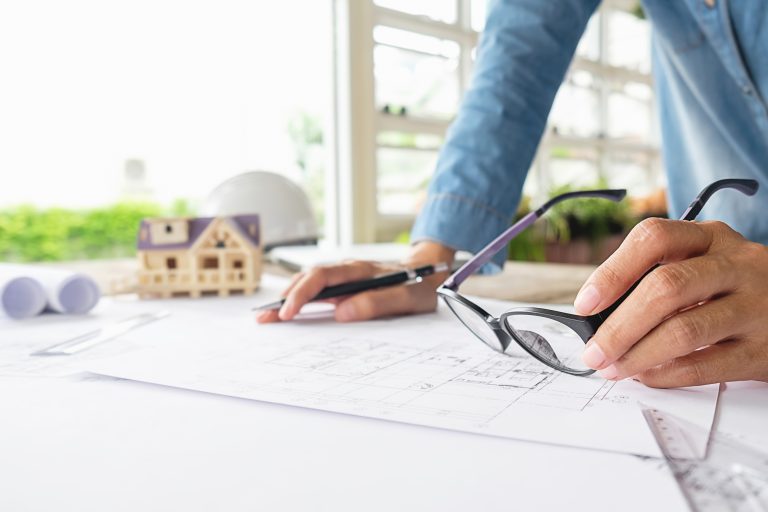 Engineer’s hands working on construction blueprint with tools.