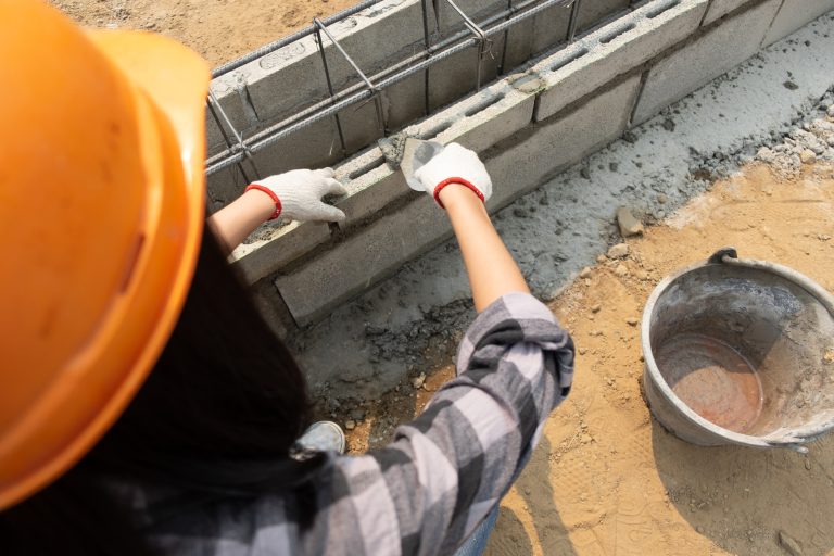 Construction worker wearing a safety helmet and gloves laying cement on concrete blocks